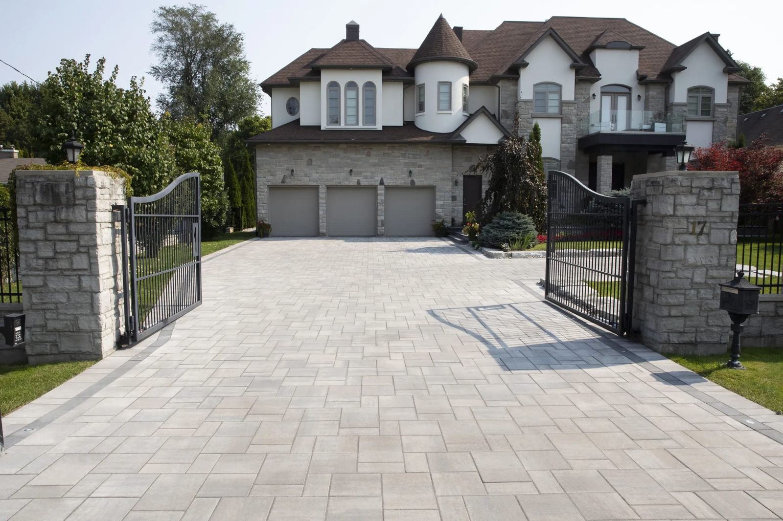 Wide paver driveway leading up to a home behind an iron gate